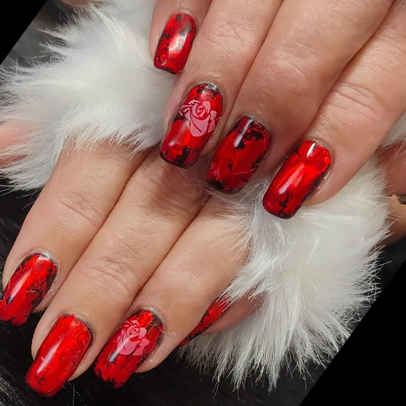 Two hands with glossy red nails and rose art feature nails, resting on white fur